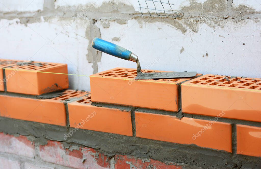 Building a cavity wall from concrete blocks and red facing bricks. An external masonry cavity wall bricklaying using a level string and a trowel.