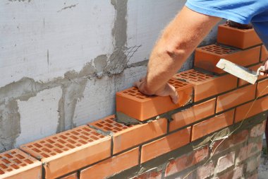 Çürük duvar inşaatı ve çukur duvar kravatları. Bir müteahhit dış duvarın tuğlalarını metal örgülü beton duvarın yanına yerleştiriyor.. 