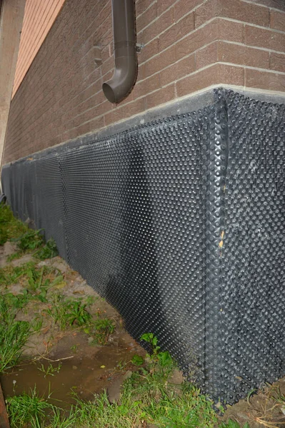 A close-up of a wet house foundation waterproofing because of a gutter downpipe installation mistake. A wet foundation damaged with water flown from a roof gutter.