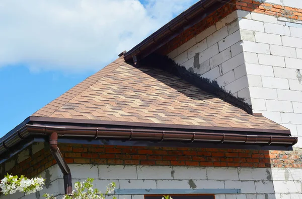 Asphalt shingles roofing construction. House asphalt shingles corner roofing construction waterproofing with roof gutter system.