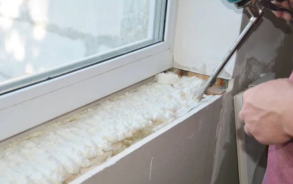 Installing window sill with caulking gun foam. House window installation indoors.