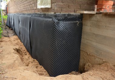 House foundation waterproofing. Installation of a dimpled waterproofing membrane on the exterior brick house basement wall. 