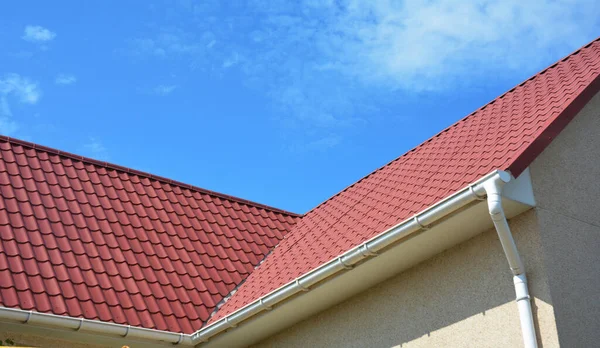 Close up on waterproofing problem area on red steel roof with raing gutters pipeline. Metal roofing corner waterproofing.