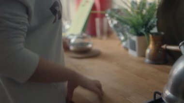 Mutfaktaki kadın çaydanlığa çay yaprakları döküyor.