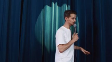 Kafkasyalı bir adamın sahnede stand-up gösterisi yaparken orta bel pozu..