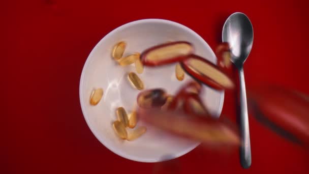 Овальні жовті таблетки потрапляють в тарілку, що стоїть на червоному столі з металевою ложкою — стокове відео