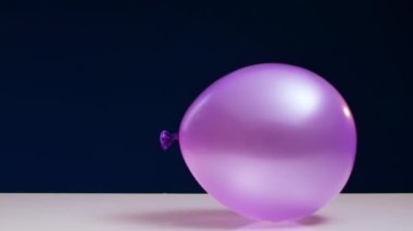 Kırmızı dart, mavi arka planda beyaz masada duran yeşil balonu şişirir.