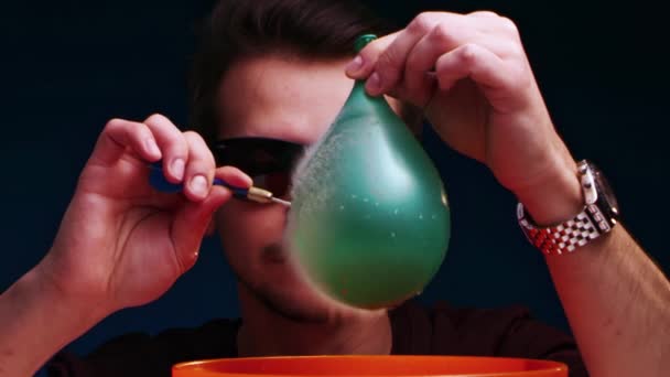 Hombre europeo en gafas de sol estalla globo de agua verde con un dardo — Vídeos de Stock