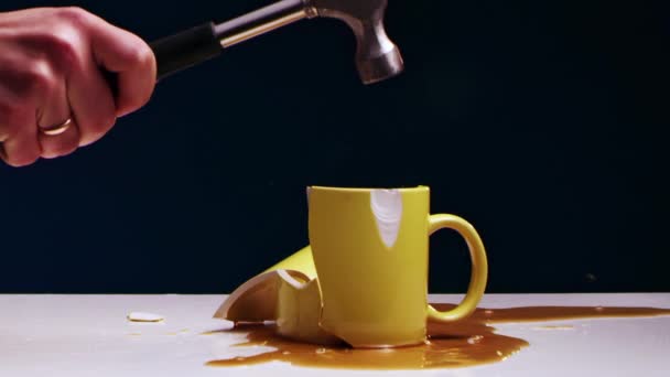 Mans mão quebra uma caneca de chá amarelo com líquido com um martelo de ferro — Vídeo de Stock