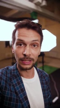 Mavi ceketli adam kayıt stüdyosundaki kameraya bir şey söylüyor.