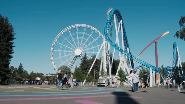 Parc d'attractions avec montagnes russes, une roue ferris par une journée d'été ensoleillée. — Video