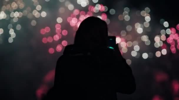 Silhouette of a woman who shoots on her smartphone multi-colored fireworks — Stock Video