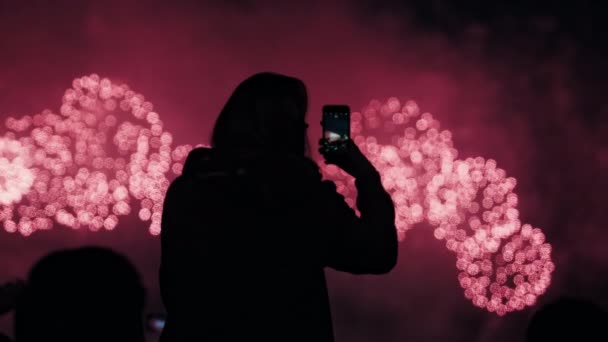 Silueta de una mujer que dispara en su smartphone fuegos artificiales multicolores — Vídeos de Stock