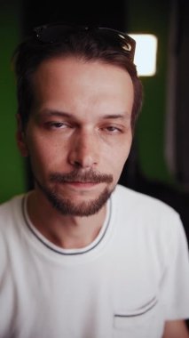 Beyaz tişörtlü adam, kayıt stüdyosundaki kameraya bir şey söylüyor.