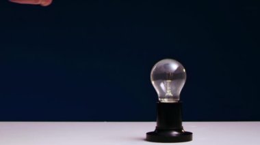 AMA 'nın eli, demir çekiçle masada duran parlak ampulü ezer..