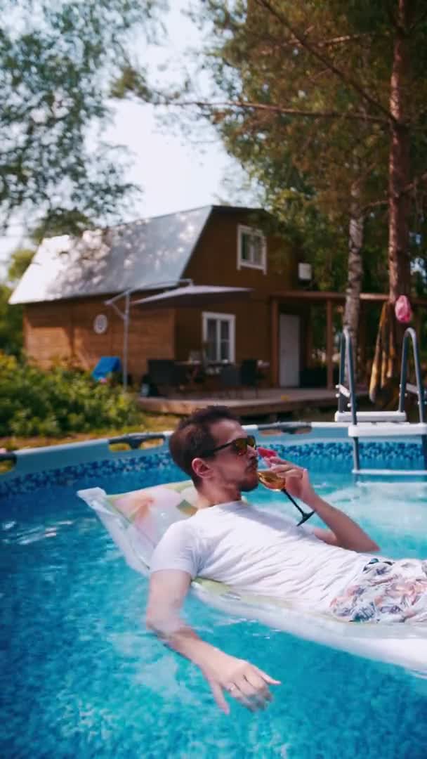 Mannen ligger på en luftmadrass i poolen med en cocktail — Stockvideo