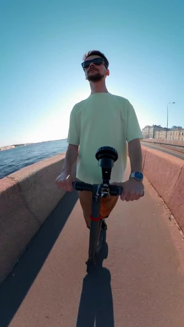 Homme monte un scooter électrique le long du remblai le long de la rivière le jour de l'été — Video