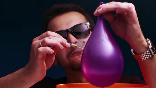 European man in sunglasses and cigarette in mouth burst purple ball with dart — Stock Video