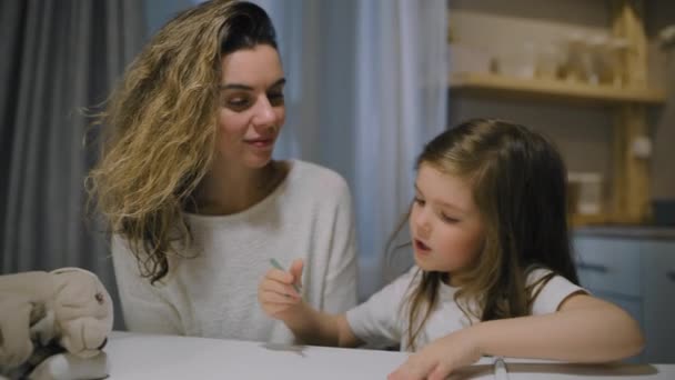 Мать и маленькая дочь рисуют на бумаге на кухне с маркерами — стоковое видео