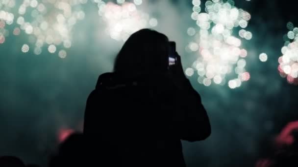 Silueta de una mujer que dispara en su smartphone fuegos artificiales multicolores — Vídeos de Stock