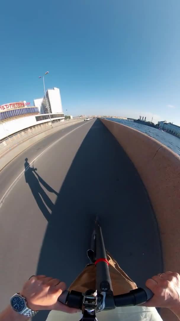 Человек ездит на электрическом скутере вдоль набережной вдоль реки в летний день — стоковое видео