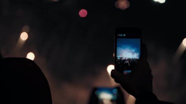 As mãos seguram smartphones e filmam vídeos de fogos de artifício explosivos no céu noturno. — Vídeo de Stock