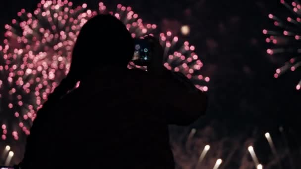 Silueta de una mujer que dispara en su smartphone fuegos artificiales multicolores — Vídeo de stock