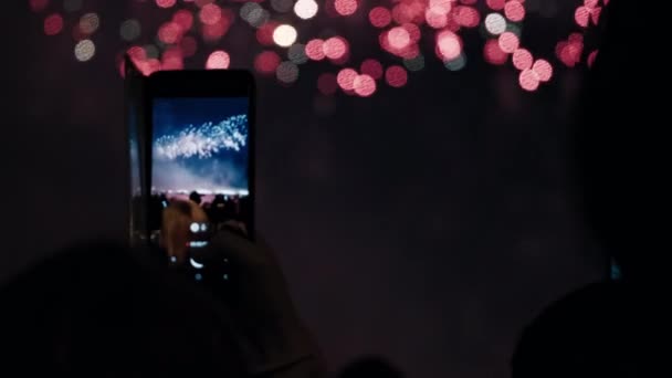 Руки тримають смартфони і знімають відео вибухівки феєрверків у нічному небі . — стокове відео