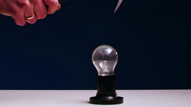 AMans hand smashes incandescent light bulb lying on table with iron hammer. — Stock Video