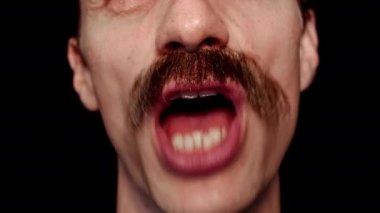 Büyük dişleri ve kırışıklıkları olan bir adam. Kıvranıyor, dilini gösteriyor, gülümsüyor ve şarkı söylüyor.