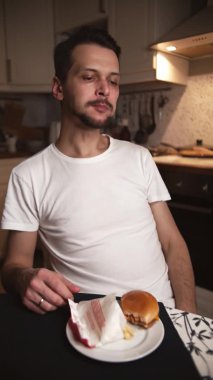 Man evening in kitchen eats hamburger and french fries from fast food. Timelapse