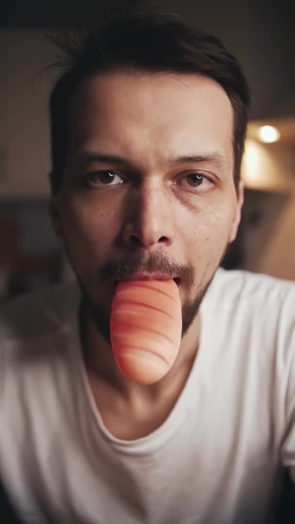 Man chews and spits out a childrens rubber toy bread and looks into the camera — Stock video