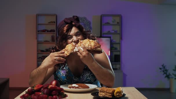 Hombre vestido de mujer vestido y maquillaje en la cara se come un sándwich enorme — Vídeos de Stock