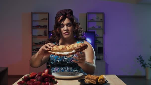 Чоловік, одягнений у жіночу сукню та макіяж на обличчі, їсть величезний бутерброд — стокове відео