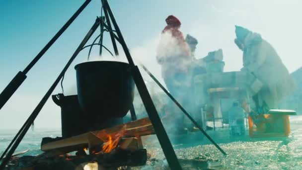 На вогні з дровами їжа готується у великих металевих кажанів на замерзлому березі річки — стокове відео