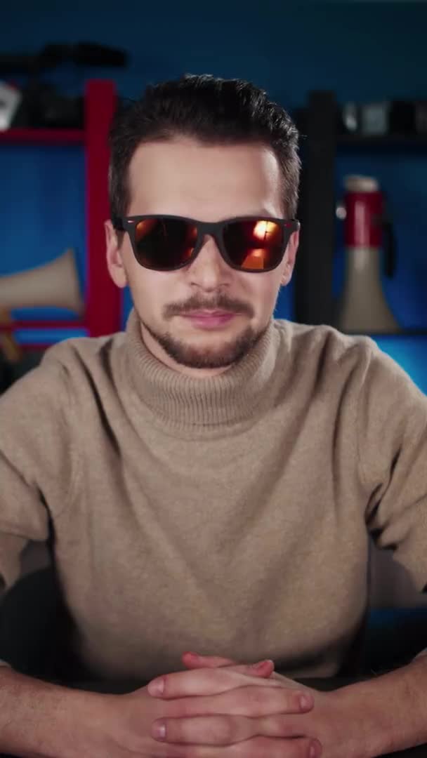 Ein Europäer mit Sonnenbrille sitzt an einem Tisch im Studio und sagt etwas — Stockvideo