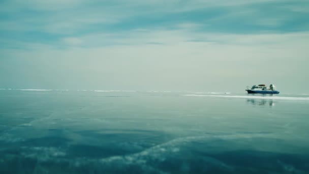 Ilmatyynyalus ratsastaa jäätyneellä järven jäällä lumipeitteisten vuorten keskellä — kuvapankkivideo