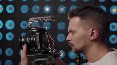 Avrupalı erkek kameraman stüdyoda çekim yapmak için bir video kamera kuruyor.