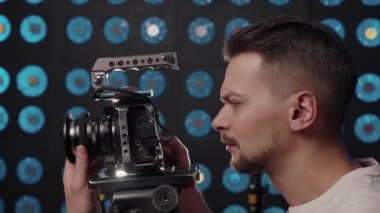 Avrupalı erkek kameraman stüdyoda çekim yapmak için bir video kamera kuruyor.