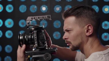 Avrupalı erkek kameraman stüdyoda çekim yapmak için bir video kamera kuruyor.
