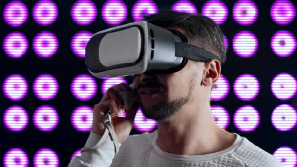 Человек в шлеме виртуальной реальности разговаривает по телефону с помощью игрового контроллера — стоковое видео