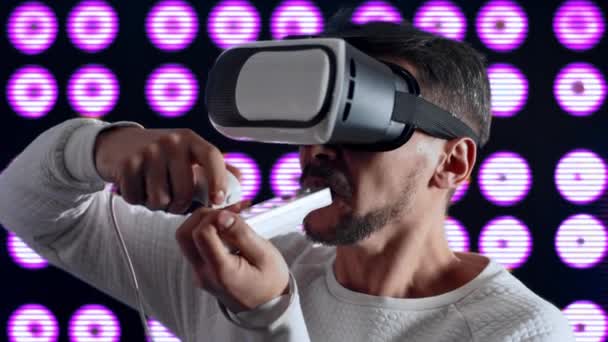 Een man in virtual reality helm steekt een sigaret aan, straalt en hoest. — Stockvideo