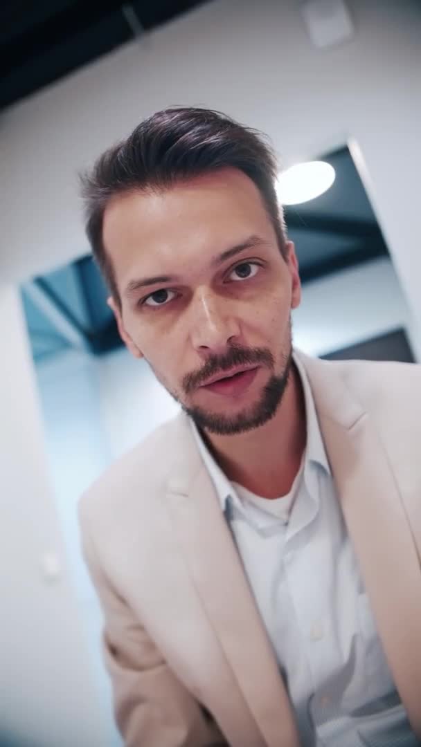 Hombre video blogger en chaqueta beige y camisa blanca, habla y mira a la cámara — Vídeo de stock