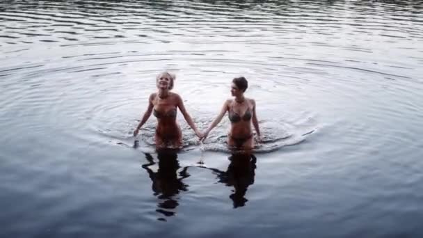 İki kadın bikini gölden çıkar, gülerek ve su sıçratarak.. — Stok video