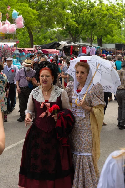 Madrid, İspanya; 15 Mayıs 2022: Saint Isidro fuarındaki tezgahları ziyaret eden bir grup insan. Sırtı dönük iki kadın geleneksel Madrid kostümü içinde 