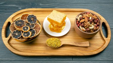 Çeşit çeşit fındık ve çeşitli kurutulmuş narenciye meyveleri ve mutfak tahtasının üzerinde taze bal peteği. İnsan vücudu için yararlı vitamin yiyeceği