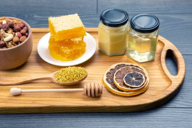 Çeşit çeşit fındık ve çeşitli kurutulmuş narenciye meyveleri ve mutfak tahtasının üzerinde taze bal peteği ve polen. İnsan vücudu için yararlı vitamin yiyeceği