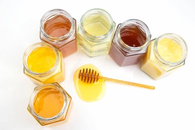 Taze ballı kaşık ve beyaz arka planda farklı bal türleri olan kavanozlar. organik vitamin yiyeceği