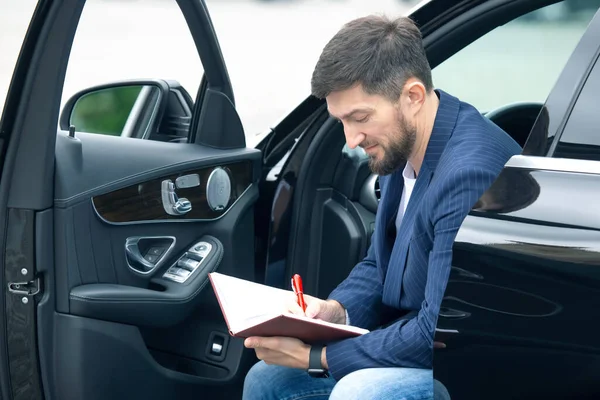 Udany Biznesmen Zajmuje Się Dokumentami Siedząc Pobliżu Swojego Prestiżowego Samochodu — Zdjęcie stockowe