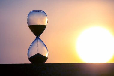 Gün batımının arka planında kum saati. Hayattaki zamanın değeri. Sonsuzluk.